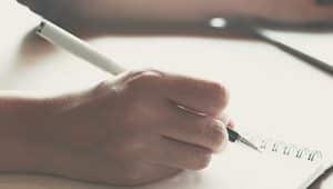 papel e caneta na mão escrevendo