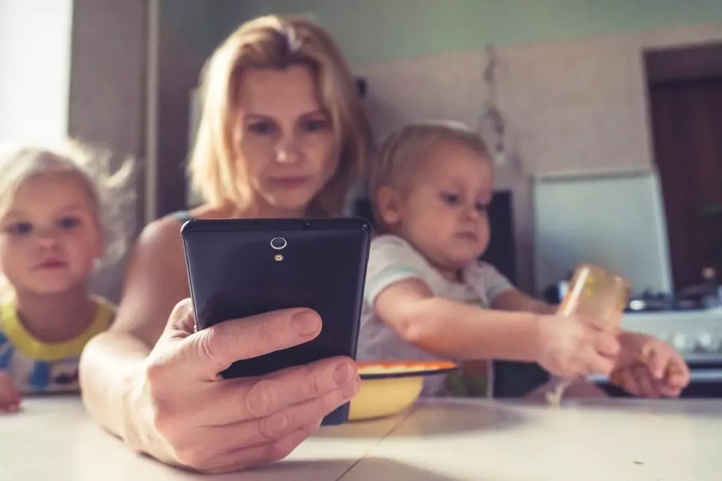 Mãe segurando celular com seus dois filhos em volta
